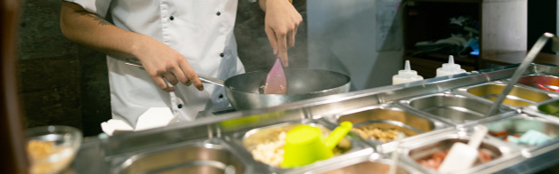 Restaurant worker in a white chef's coat cooking in a kitchen.