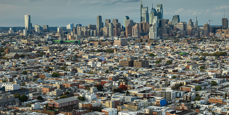 Tall buildings loom in the distance and are surrounded by many blocks of row homes in the city of Philadelphia, PA.