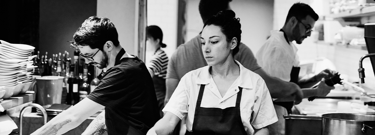 Employees in a restaurant kitchen wearing aprons.