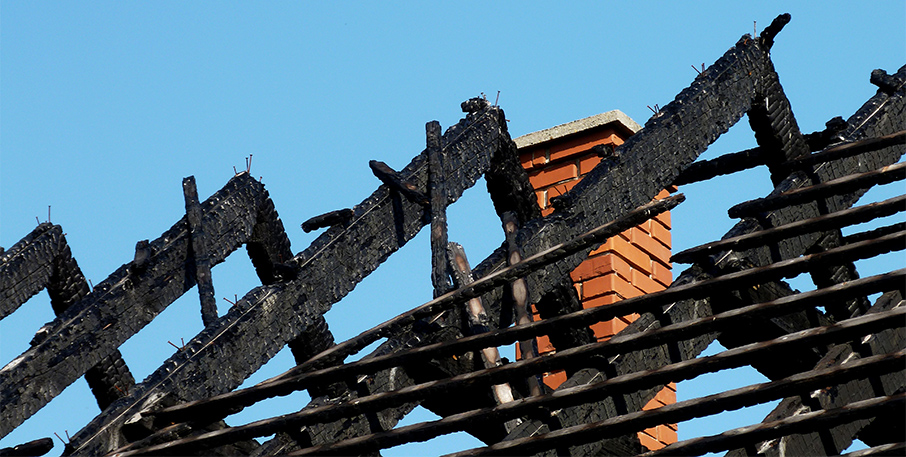 A brick chimney stands behind a burnt roof.