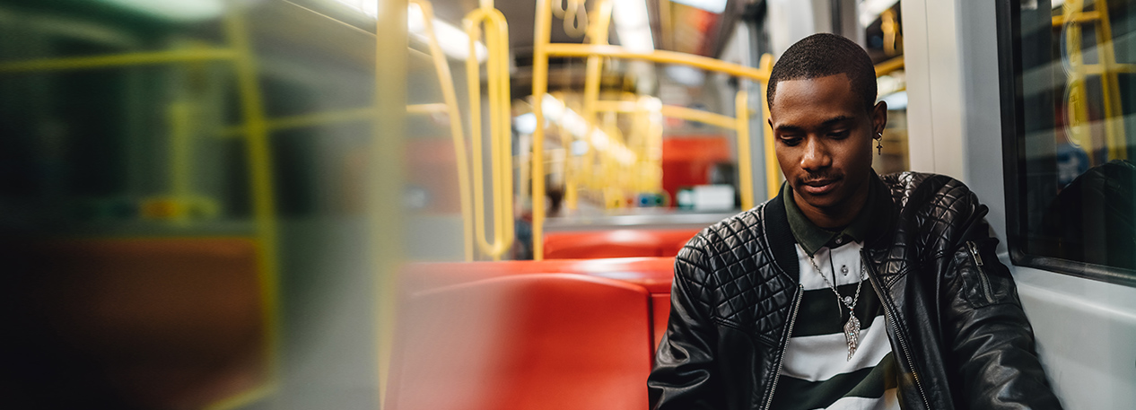 A man sits alone in a subway car scrolling on his smartphone.